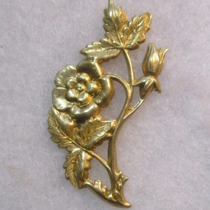 May include: A gold-toned metal rose with leaves and a bud. The rose is detailed and has a realistic look.