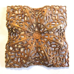 May include: A square, ornate, metal embellishment with a filigree design. The embellishment is made of brass and has a gold finish.