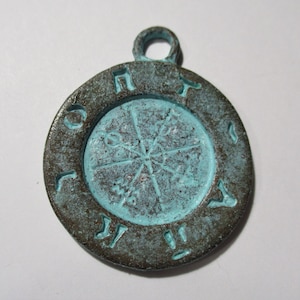 May include: A teal blue and brown metal pendant with a circular design and runes around the edge.