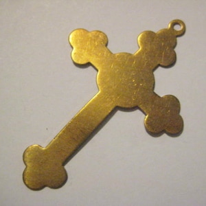 May include: A gold-colored metal cross pendant with a simple design. The cross has a rounded center and four rounded arms.