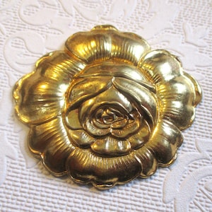 May include: A gold-colored metal rose flower embellishment. The rose is detailed with a raised center and petals.