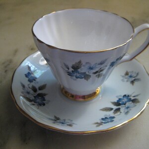 May include: A white teacup and saucer with a gold trim and blue floral pattern.