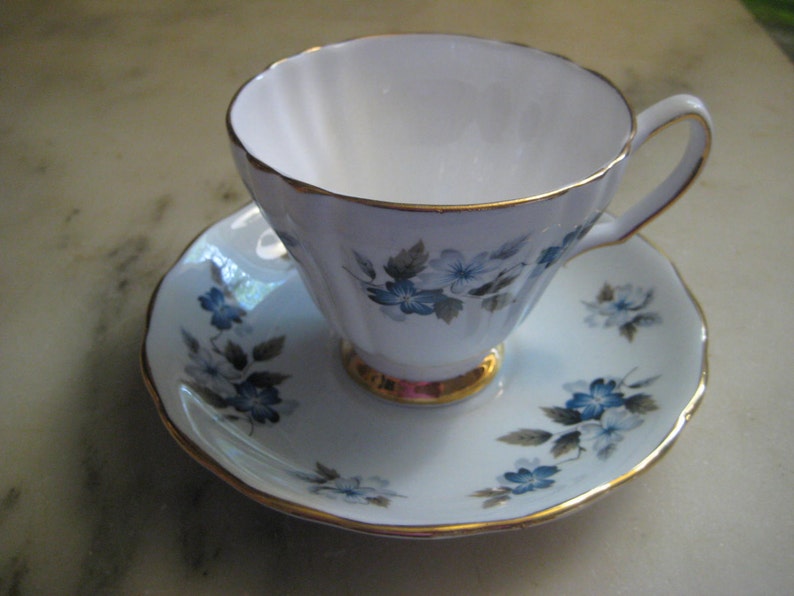 May include: A white teacup and saucer with a gold trim and blue floral pattern.