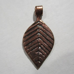 May include: A copper leaf pendant with a textured design. The pendant has a loop at the top for attaching to a chain or cord.