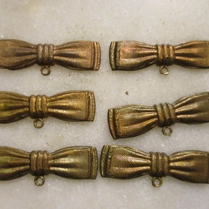 May include: Six gold-toned bow tie shaped metal embellishments with a loop at the bottom.