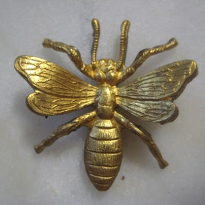 May include: A gold-colored metal bee brooch with detailed wings and a textured body.