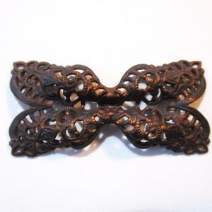 May include: A decorative metal butterfly-shaped embellishment with an intricate, openwork design. The piece is made of a dark, aged metal with a slightly reddish hue.