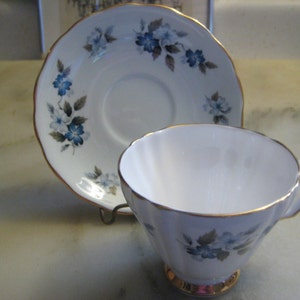 May include: A white teacup and saucer with a blue and gray floral pattern and gold trim.