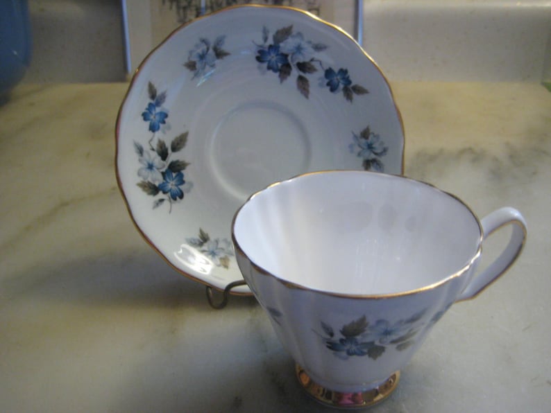 May include: A white teacup and saucer with a blue and gray floral pattern and gold trim.
