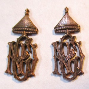 Może przedstawiać: Dwa antyczne złote broszki z koroną i literami "N.G." w ozdobnym kroju.