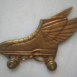 May include: A bronze-colored roller skate with wings. The skate features a classic design with four wheels and is adorned with detailed wings, giving it a vintage or retro aesthetic. The wings are positioned on the side of the skate.