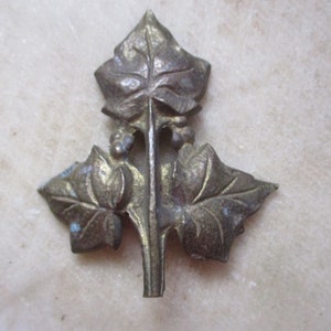 May include: A gold-toned metal leaf design with three leaves and a stem. The leaves are detailed with veins and have a slightly aged look.