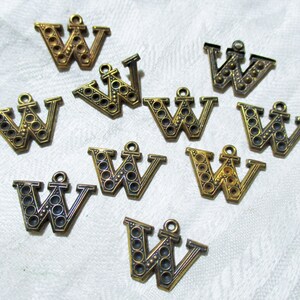 May include: Ten gold-colored metal charms shaped like the letter W. Each charm has a raised design of small circles around the letter. The charms have a loop at the top for attaching to a necklace or bracelet.