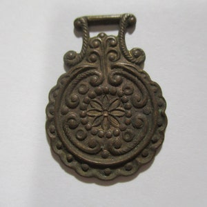 May include: Ornate bronze-colored metal decorative piece with a floral design. The piece features a central flower surrounded by circular patterns and a scalloped edge. A loop is at the top for hanging. The piece is approximately 3 inches long.