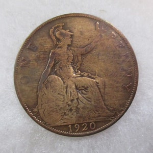 May include: A copper-colored coin featuring a seated woman with a helmet, holding a staff. The coin is inscribed with the word "PENNY" and the year "1920". The coin has a worn appearance, with visible signs of age and use.