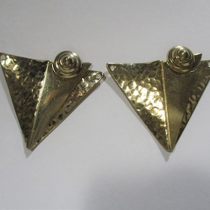 Könnte beinhalten: Ein Paar goldfarbene, geometrische Ohrringe. Jeder Ohrring hat eine strukturierte, gehämmert-metallische Dreiecksform mit einem Spiraldetail oben. Die Ohrringe haben kleine Löcher zur Befestigung.