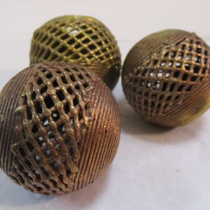 May include: Three decorative metal spheres with a lattice design. The spheres have a bronze and gold finish, with a textured surface. The spheres are arranged on a white surface.