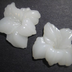 May include: Two white ceramic flower-shaped embellishments. The flowers have five petals and a center hole.