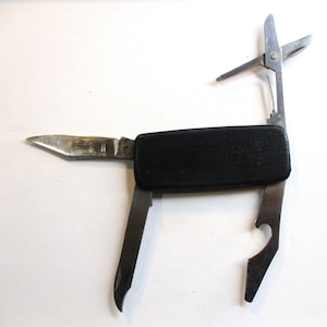 Könnte beinhalten: Ein Taschenmesser mit schwarzem Griff und verschiedenen Werkzeugen, darunter eine Klinge, eine Schere, ein Flaschenöffner und ein Flachkopf-Schraubendreher.