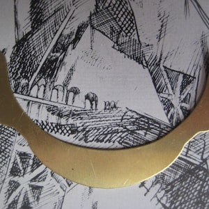 May include: A gold-colored metal crescent-shaped piece with two small holes at the top.