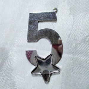 May include: A silver metal ornament shaped like the number 5 with a star in the center.