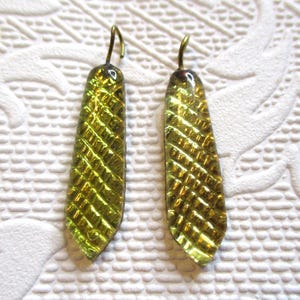 May include: A pair of gold and green glass earrings with a textured pattern. The earrings are teardrop shaped and have a hook closure.