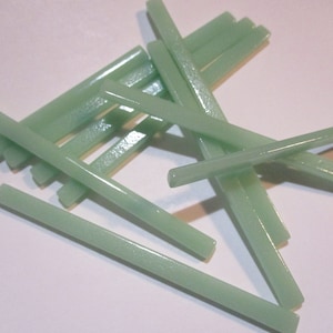 Puede incluir: Un grupo de varillas de vidrio verde claro, dispuestas en forma de cruz. Las varillas miden aproximadamente 1,2 cm de ancho y 15 cm de largo.