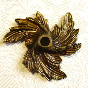 May include: A gold-toned metal decorative accent with a swirling, leaf-like design. The accent has a hole in the center for attaching to a surface.