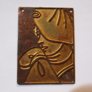 Peut inclure: Une plaque en métal de couleur cuivre avec un motif en relief d'une personne tenant un petit animal. La plaque a deux trous en haut pour la suspendre.