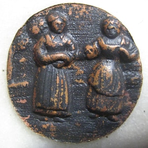 May include: A copper-colored metal medallion with two figures in relief. The figures are dressed in long robes and appear to be interacting with each other. The medallion has a worn, aged appearance.