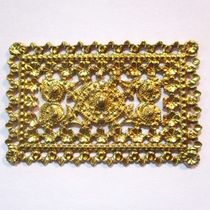 May include: A gold-colored metal decorative trim with a square shape and intricate floral designs. The trim has a raised, textured surface and a delicate, scalloped edge.