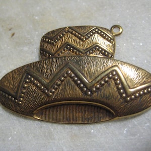 May include: Gold-toned metal pendant shaped like a hat with a zig-zag pattern and a textured surface.