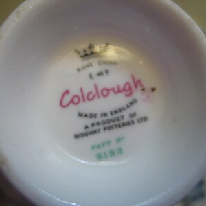 May include: Close-up of the bottom of a white teacup with a pink and black logo that reads "Colclough" and the text "Made in England A product of Ridgway Potteries Ltd.  Pat. No. 8188".