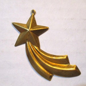 May include: A gold-colored metal ornament shaped like a shooting star. The star has five points and a long tail with three stripes.