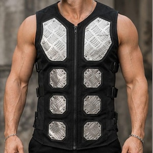 May include: Black tactical vest with silver diamond plate accents. The vest features a V-neck, a full-length zipper, and adjustable straps. The vest has six diamond-shaped metal plates and is worn over a black shirt and pants.