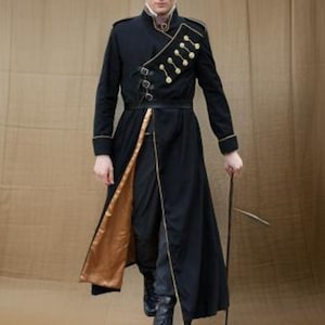May include: A black military-style coat with gold accents, including buttons and trim. The coat has a high collar and a split front revealing a gold lining. The person is holding a thin, dark rod.
