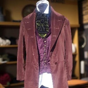 May include: A burgundy velvet coat with a double-breasted design, paired with a purple vest and a patterned ascot. The outfit includes a white collared shirt and black trousers, creating a vintage aesthetic.