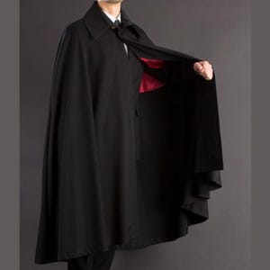 May include: A black cape with a collar and a red satin lining. The cape is open, revealing the lining and the person's attire underneath. The cape is made of a smooth, flowing fabric.