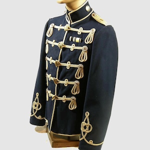 Könnte beinhalten: Marineblaue Jacke im Militärstil mit goldfarbenen Verzierungen und dekorativen Elementen. Die Jacke hat einen hohen Kragen, goldfarbene Seildetails und goldfarbene Knöpfe. Lange Ärmel und schwerer Stoff deuten auf ein formelles Kleidungsstück hin.