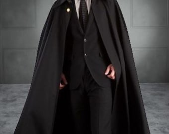 Könnte beinhalten: Ein schwarzer Umhang mit passendem Anzug. Der Umhang hat einen breiten Kragen und einen goldfarbenen Knopf. Der Anzug umfasst ein weißes Hemd mit Kragen und eine schwarze Krawatte. Das Outfit ist formell und elegant.