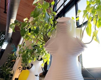 Op de afbeelding: Een witte, verticaal geribbelde, meerlaagse hydrocultuur plantenbak met een taps toelopend silhouet. De structuur heeft meerdere ronde openingen aan de zijkanten, elk met een groene bladplant met zichtbare stengels en bladeren.