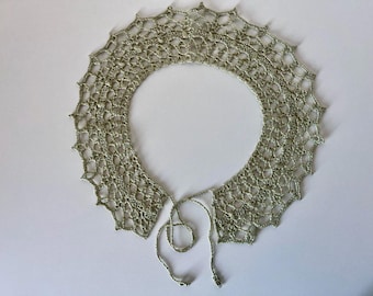 May include: A delicate, sage green crocheted collar with a scalloped edge. The openwork design features a repeating pattern of small holes, and it has a tie closure at the front. The collar is likely handmade.