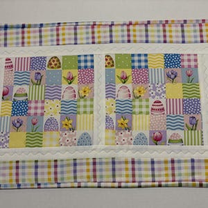 Pode incluir: Esteira de P&aacute;scoa com um design de patchwork. O centro apresenta quadrados com ovos de P&aacute;scoa, flores e padr&otilde;es em cores pastel. Uma borda branca com vieiras emoldura o centro, e uma borda xadrez em tons pastel envolve toda a esteira.