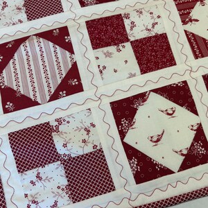 May include: A patchwork quilt featuring a repeating pattern of cream and deep red fabric squares. The design includes blocks with floral prints, stripes, and motifs of birds and bees. Each square is separated by cream sashing with red rickrack.