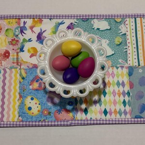 Może przedstawiać: Prostokątna podkładka pod talerz w tematyce wielkanocnej z patchworkowym wzorem z pastelowymi wzorami i białą, karbowaną miseczką wypełnioną kolorowymi jajkami. Podkładka ma fioletową obw&oacute;dkę w kratkę vichy.