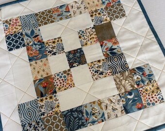 Peut inclure: Une pièce de tissu matelassée carrée présentant un motif en patchwork composé de divers imprimés floraux et géométriques dans des tons de bleu, crème, beige et orange. L'ouvrage est constitué de carrés crème unis alternés avec des carrés à motifs, bordé d'une bordure bleu foncé et de surpiqûres en losange.
