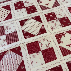 May include: A patchwork quilt featuring a repeating grid of square blocks in deep red and cream. The design alternates between four-patch floral patterns, polka dots, stripes, and cream squares printed with small red bees, all joined by wavy stitching.