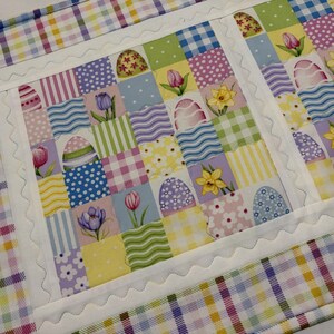 Pode incluir: Um caminho de mesa de P&aacute;scoa acolchoado com um design de patchwork. O centro apresenta quadrados com ovos de P&aacute;scoa, tulipas e narcisos. A borda &eacute; um padr&atilde;o xadrez colorido. O caminho de mesa tem cerca de 36 cm de largura e 102 cm de comprimento.
