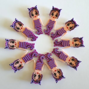 May include: Ten purple and pink cat-themed resin charms with striped patterns and black eyes. The charms are arranged in a circle.