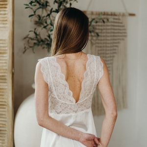 May include: White satin nightdress with a lace back. The nightdress features a V-neck and cap sleeves. The back is open, showing the wearer's back. The nightdress is floor-length and made of a soft, flowing fabric.